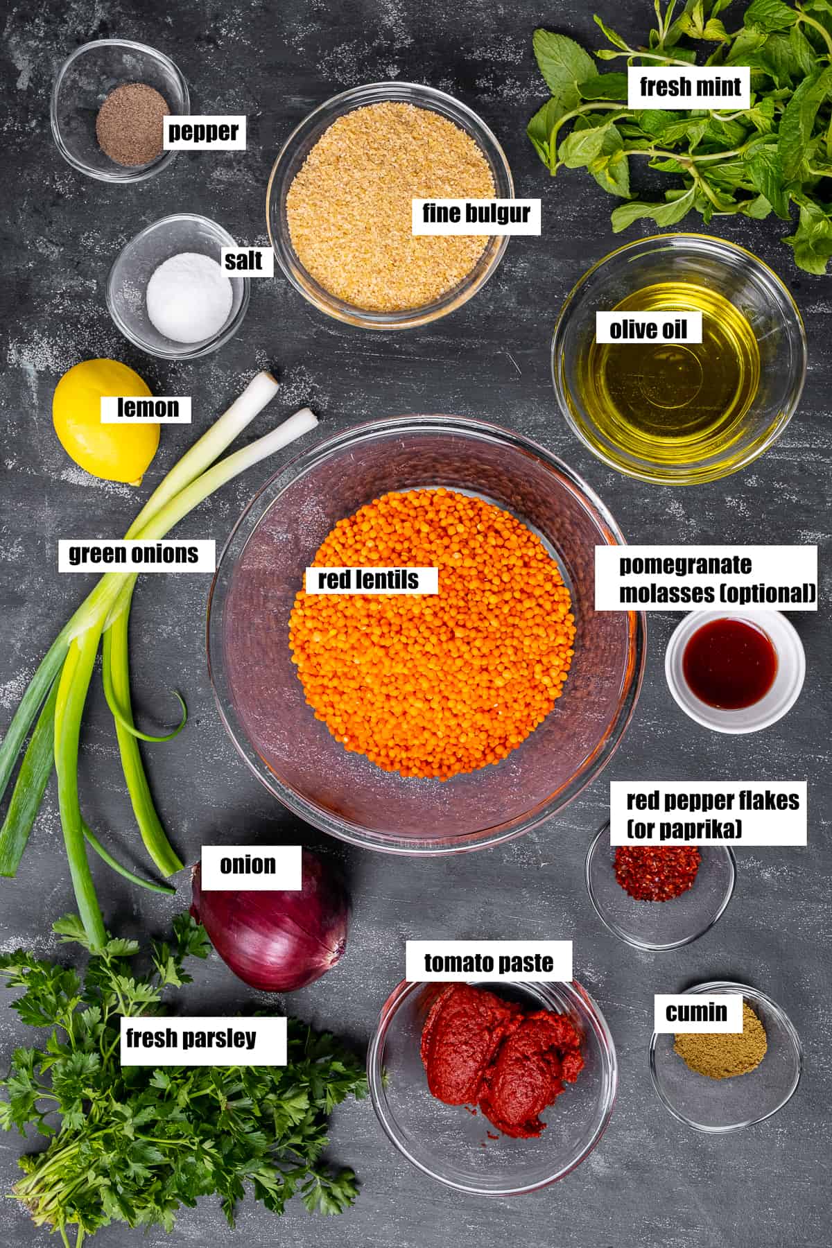 Red lentils, bulgur, oil, spices, herbs, tomato paste, lemon on a dark background.