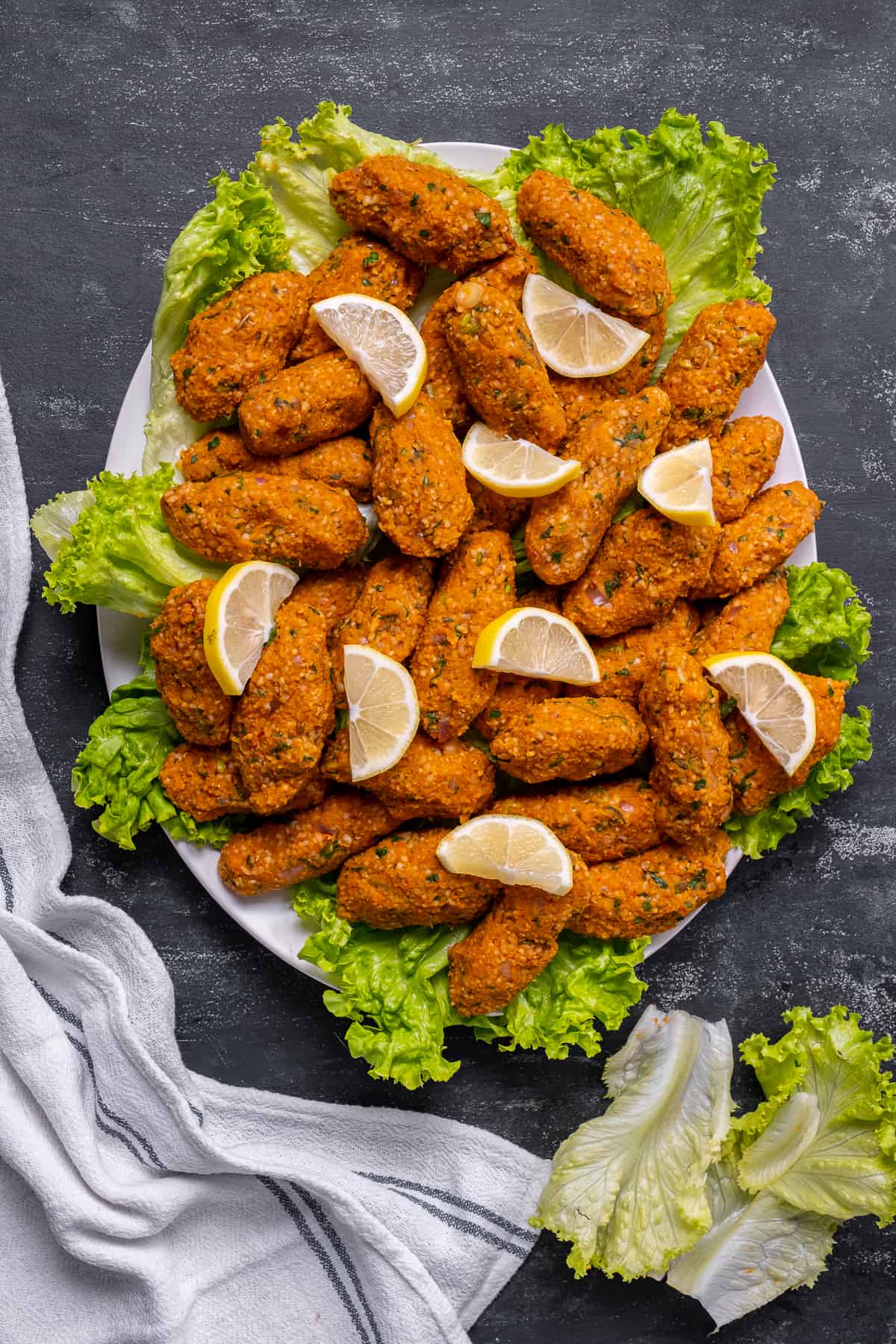 Mercimek koftes served on lettuce leaves and garnished with lemon slices on an oval plate.