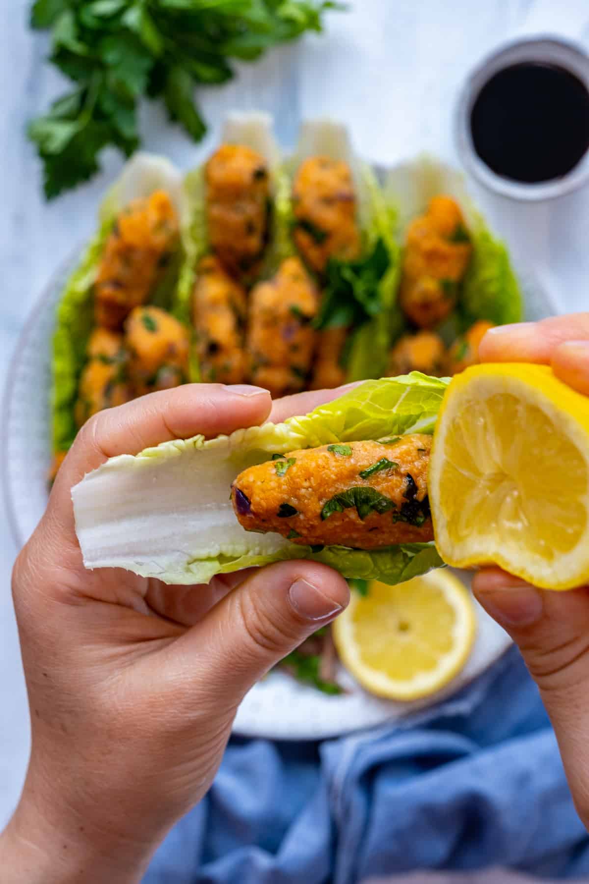 Hands holding a mercimek koftesi in a lettuce leaf and squeezing lemon over it.