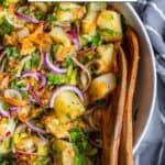 Potato salad with herbs in a white bowl and wooden spoons inside it.