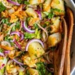 Turkish potato salad with boiled potatoes, red onion, grated carrot, herbs, and olive oil dressing in a bowl with wooden salad servers.