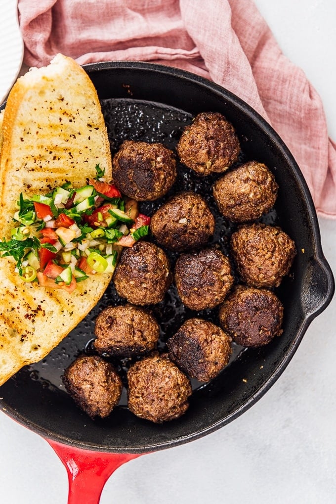 Turkish kofta and a slice of toasted bread topped with salad in a cast iron pan.