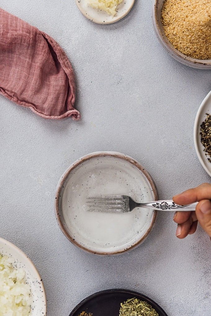 Hands whisking baking soda, lemon juice and water in a small ceramic bowl.