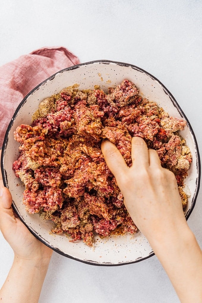 Hands mixing Turkish kofta ingredients in a ceramic bowl.