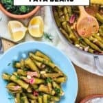 Turkish-style fava beans in pods in a blue bowl, garnished with fresh dill, with a pan of the dish, lemon halves, and yogurt on the side.