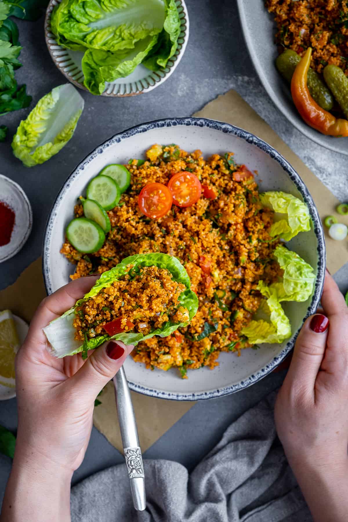 Woman about to eat bulgur salad in a lettuce leaf and a bowl of salad on the side.