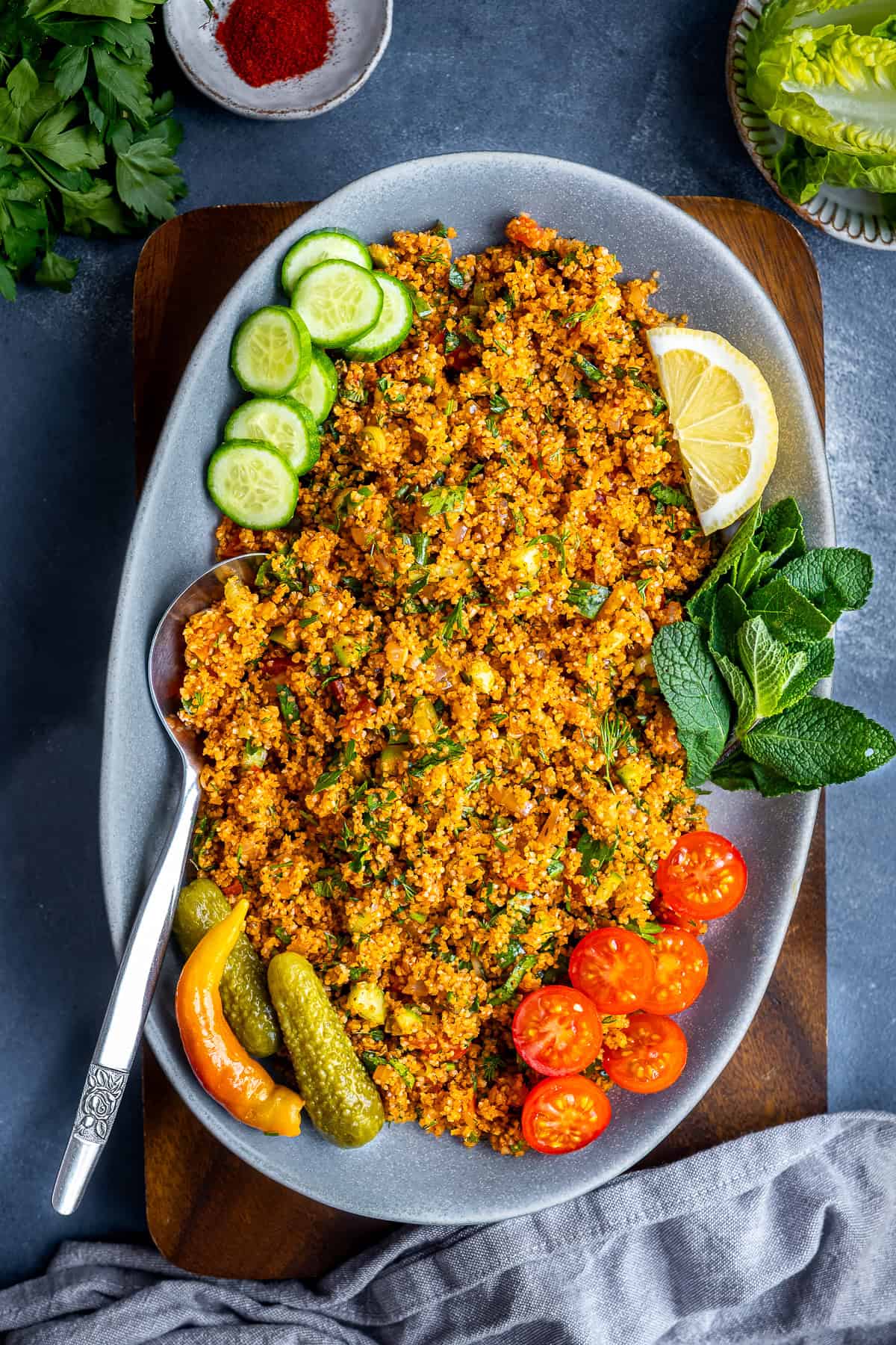 Platter of Turkish kisir served with cucumber slices, cherry tomatoes, pickles, lemon wedges, and fresh mint leaves.