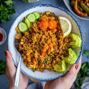 A bowl of Turkish kisir made with fine bulgur, herbs, tomatoes, and cucumbers, served with lemon wedges, lettuce leaves, and cucumber slices.