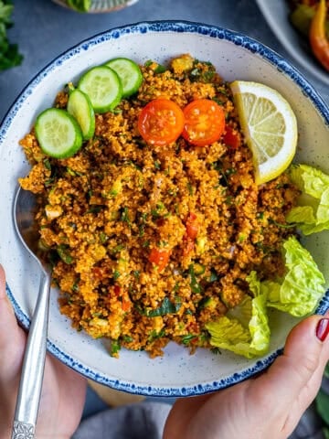 A bowl of Turkish kisir made with fine bulgur, herbs, tomatoes, and cucumbers, served with lemon wedges, lettuce leaves, and cucumber slices.