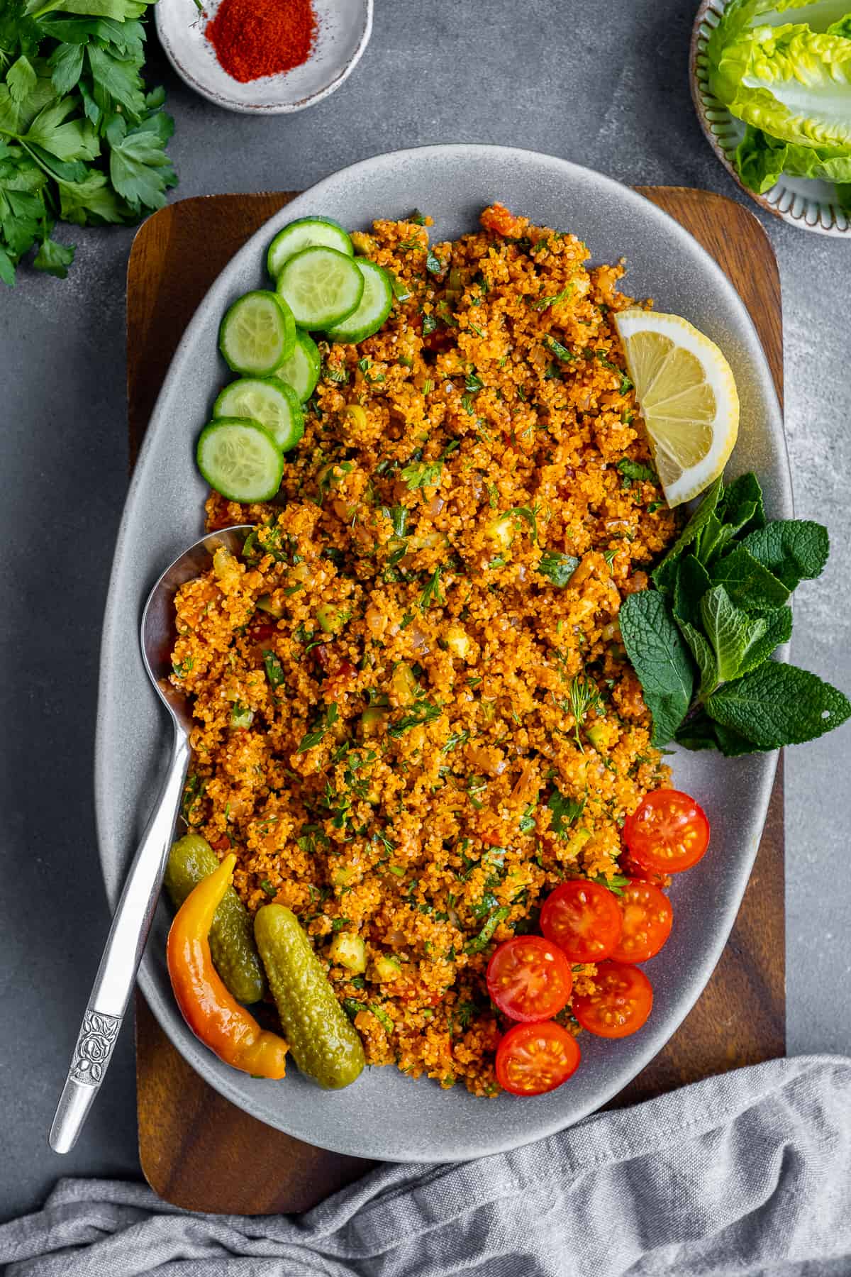 Bulgur wheat salad garnished with fresh mint leaves, pickles, sliced cucumber and tomaotes in an oval plate.