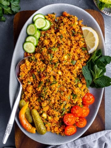 Bulgur salad garnished with fresh mint leaves, pickles, sliced cucumber and tomaotes in an oval plate.