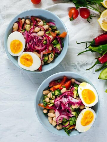 White bean salad garnished with pickled onions and hard boiled eggs in two bowls.