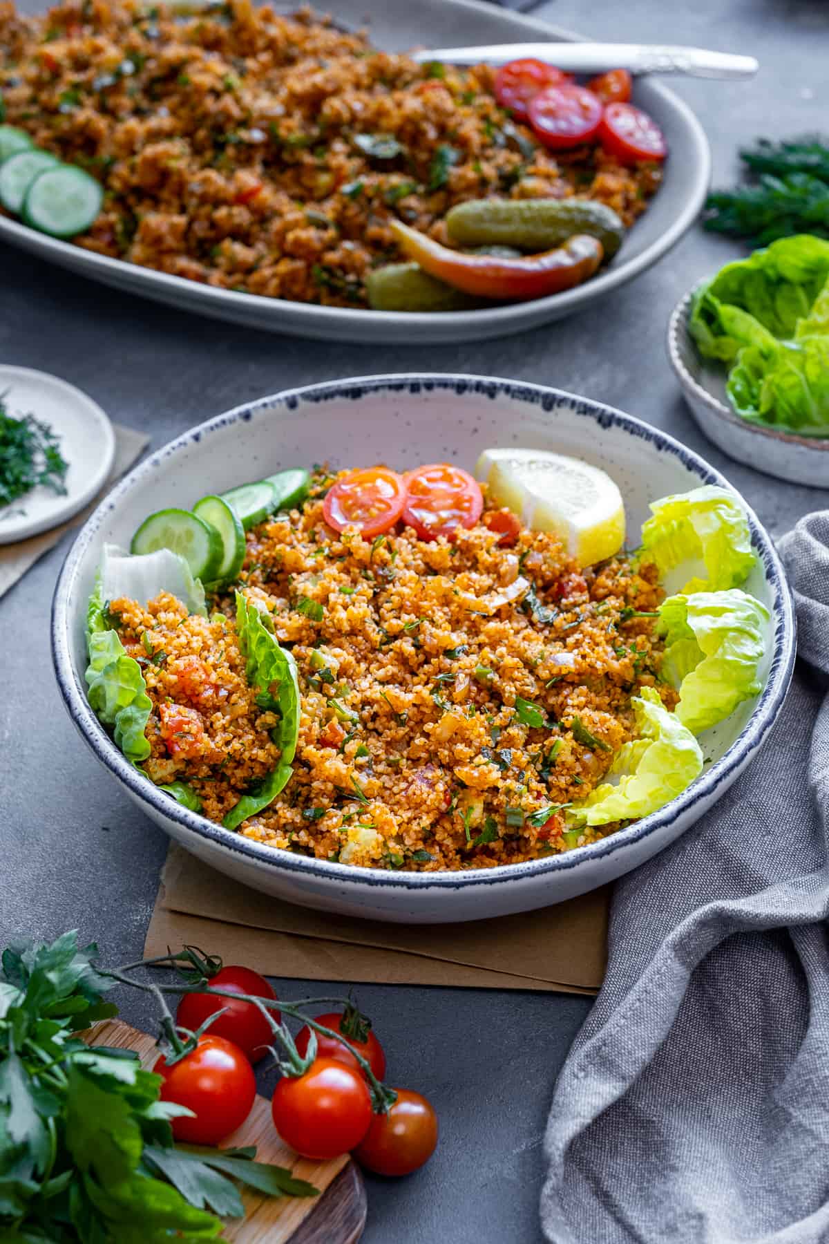 Bulgur salad in a bowl, lettuce leaves on it and another plate loaded with bulgur salad behind it.