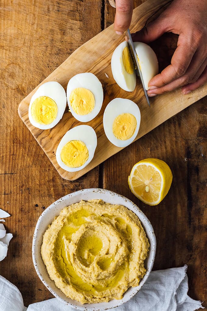 Halved hard boiled eggs on a cutting board and a bowl of hummus to make healthy deviled eggs