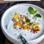A bowl of cacık garnished with olive oil, diced cucumber, dried mint, pul biber, sumac and fresh mint leaves.