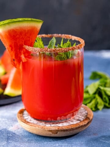 Watermelon margarita in a small glass garnished with a small slice of watermelon and mint leaves.