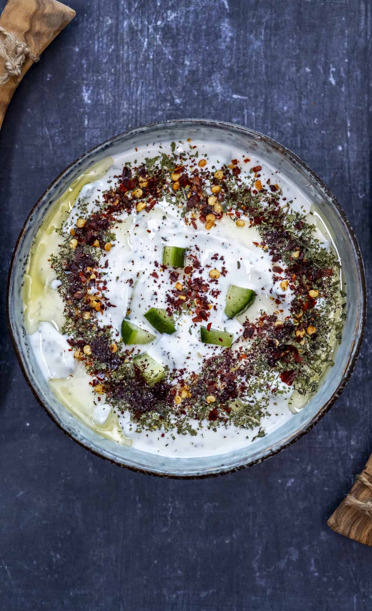 Cacik garnished with spices in a bowl on a dark background.