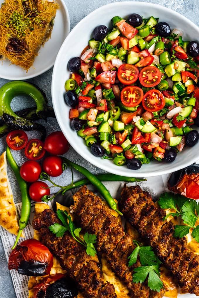 Turkish shepherd salad with tomatoes, cucumbers, onions and olives served in a large bowl and Turkish kabob on the side.