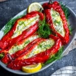Feta cheese stuffed peppers garnished with fresh dill and lemon slices on an oval serving plate.