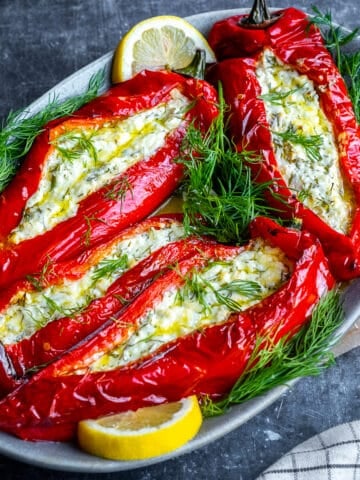 Feta cheese stuffed peppers garnished with fresh dill and lemon slices on an oval serving plate.