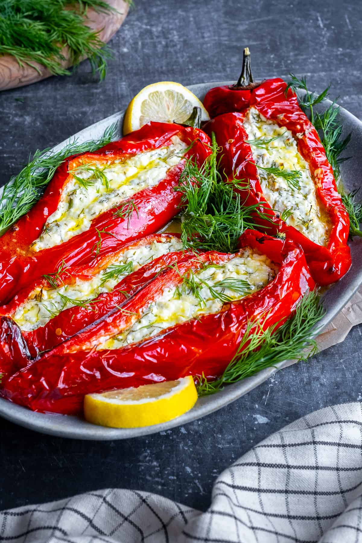 Feta stuffed red peppers garnished with fresh dill and lemon slices on an oval plate.