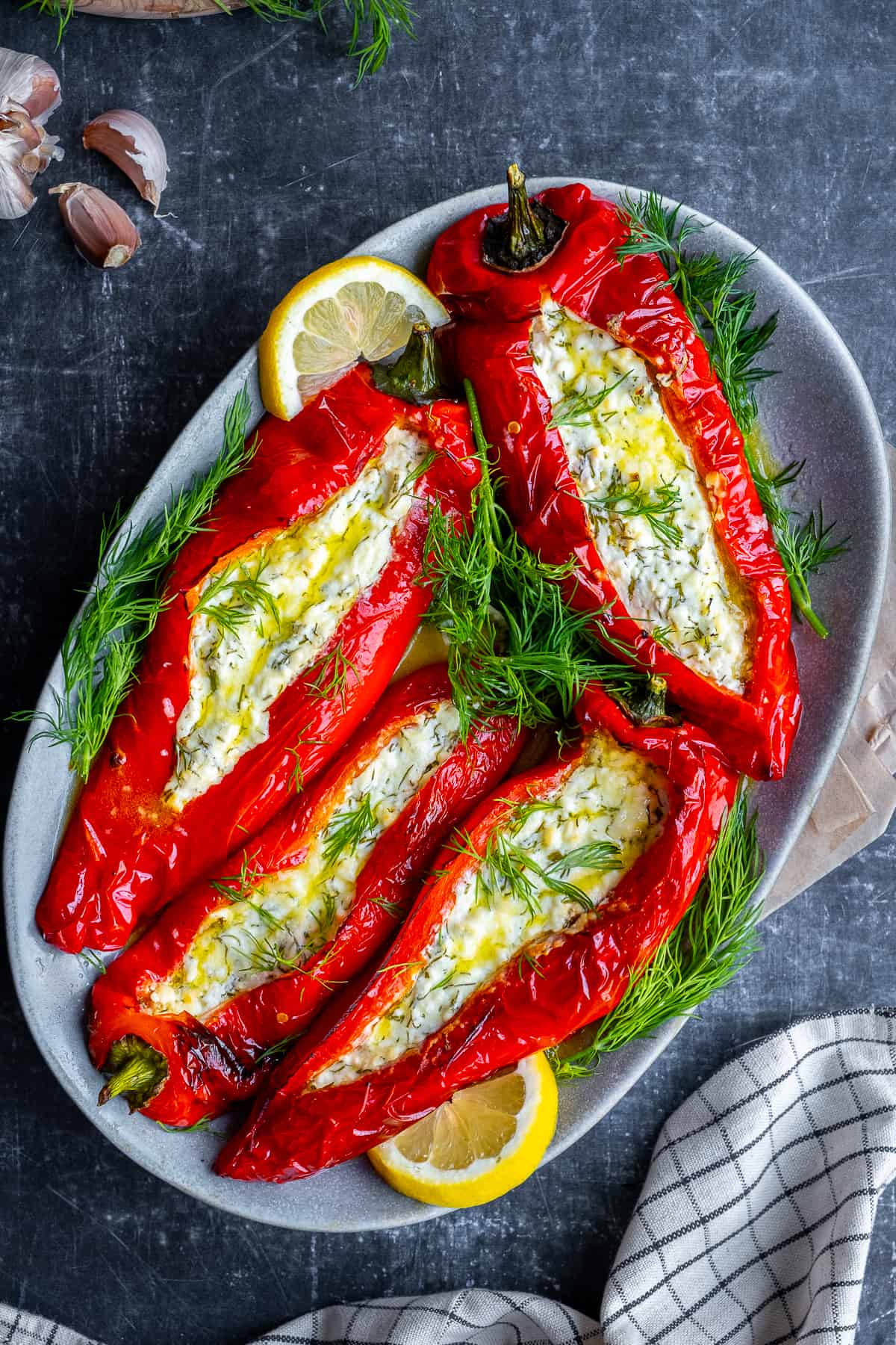 Feta cheese stuffed red peppers garnished with fresh dill and lemon slices on an oval serving plate photographed from top view.