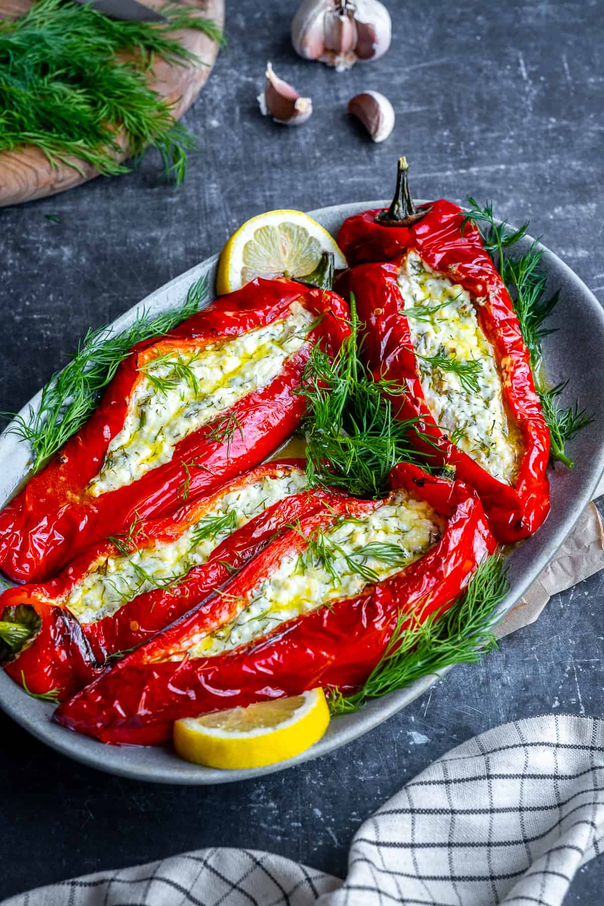 Feta stuffed red peppers garnished with fresh dill and lemon slices on an oval plate.