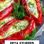 Roasted red peppers stuffed with feta cheese and herbs, garnished with fresh dill and served with lemon slices on a plate.