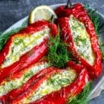 Feta stuffed roasted red peppers on a serving plate, garnished with dill and lemon, with a rustic background.