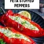 Feta stuffed roasted red peppers on a dark plate, garnished with dill, with garlic and herbs in the background.