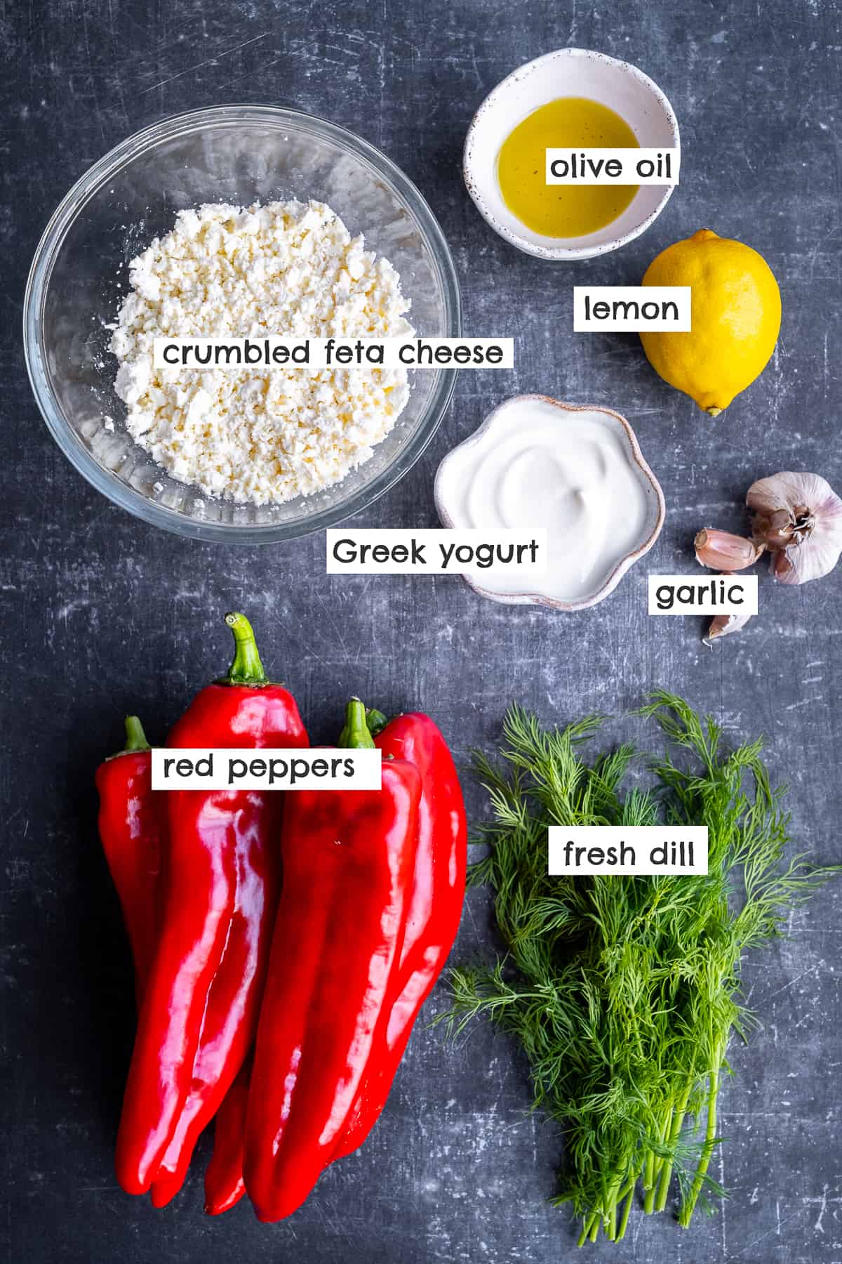 Romano peppers, fresh dill, crumbled feta cheese, yogurt, lemon, garlic cloves, olive oil on a dark background.