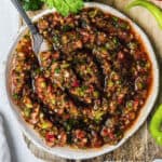 Turkish ezme salad on a white ceramic plate with a fork inside it. A bunch of parsley and a slice of lemon on the side.