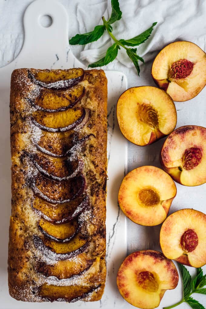 Fresh peach bread with peach slices on a white cutting board