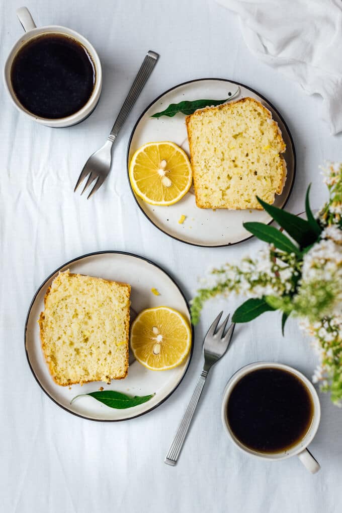 Lemon zucchini cake slices on two plates accompanied by two cups of coffee. 