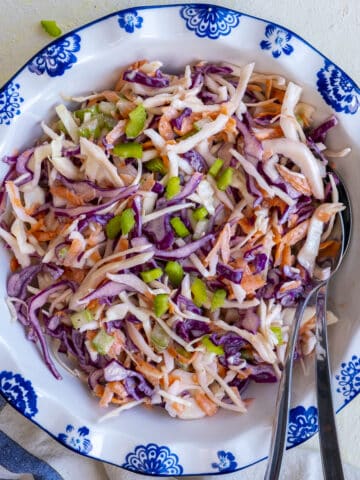 Healthy coleslaw in a white bowl and spoons inside it.
