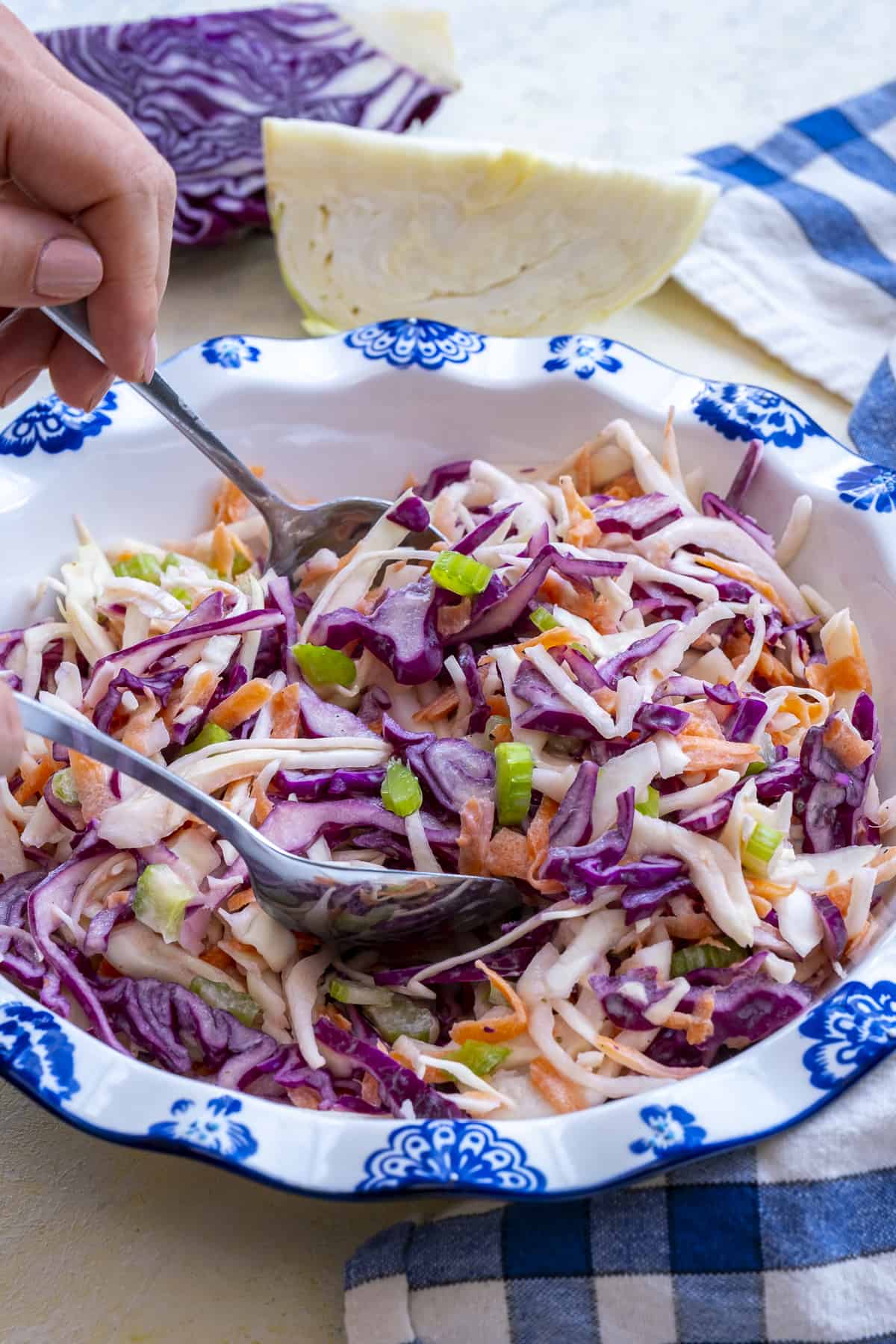 Hands tossing coleslaw mixture in a white bowl.