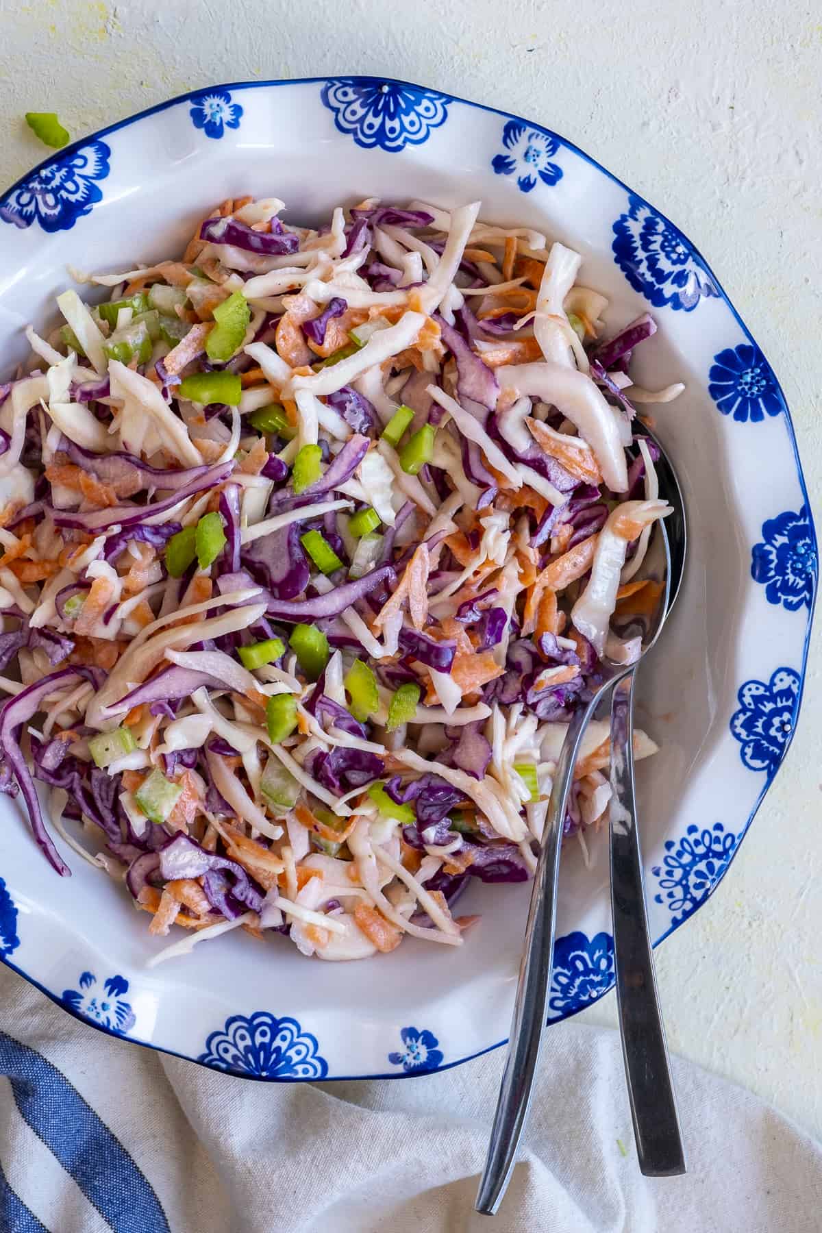 Yogurt coleslaw in a white bowl and two spoons inside it.