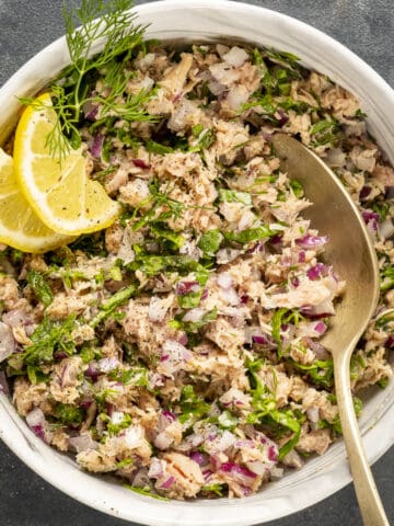 Tuna salad garnished with lemon wedges and fresh dill served in a white bowl.