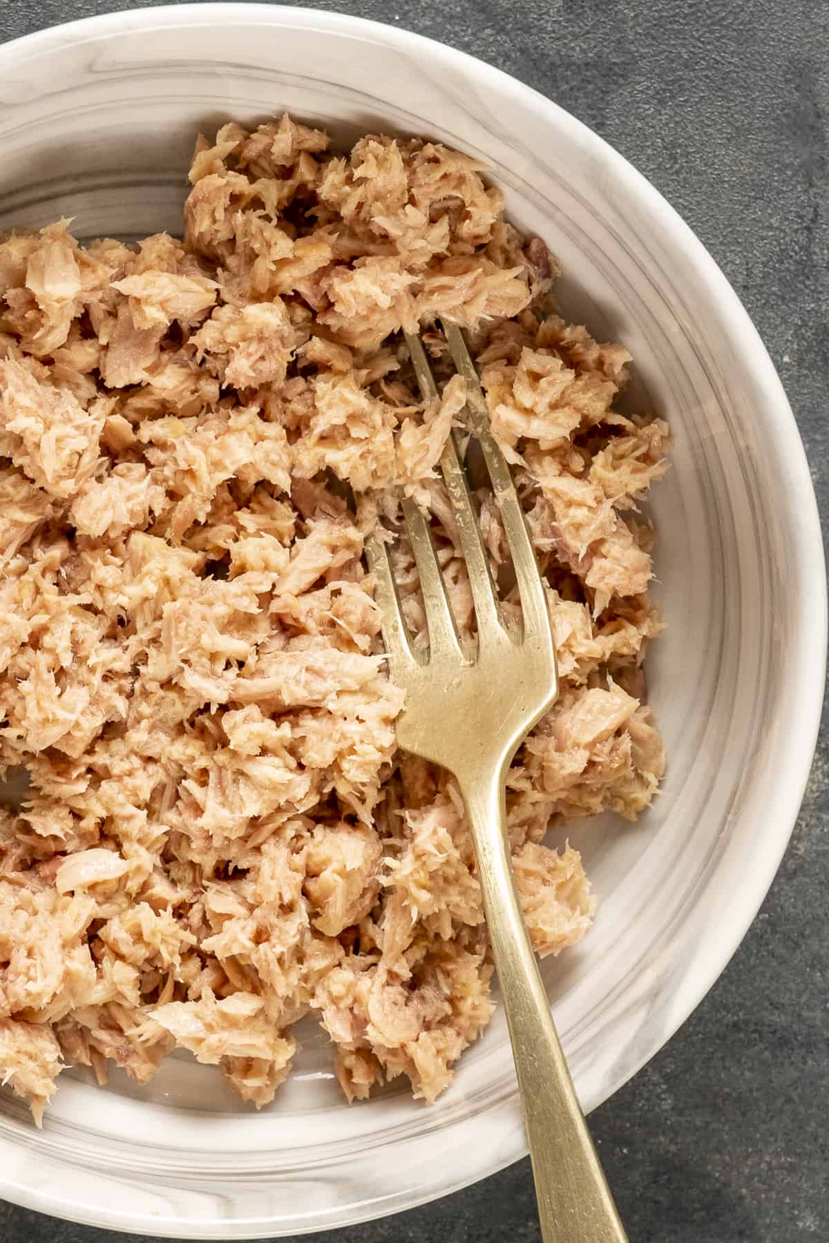Flaked tuna meat in a white bowl and a fork inside it.