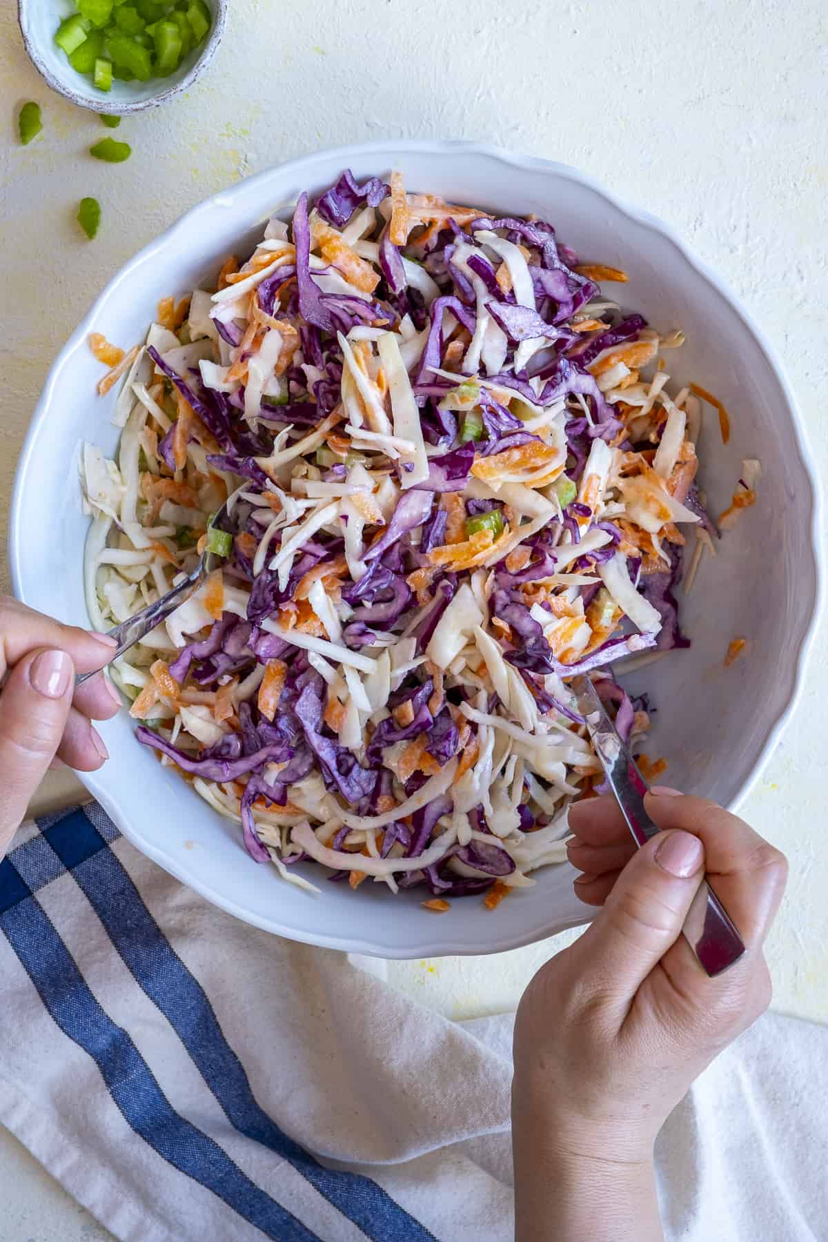 Hands tossing coleslaw base with yogurt dressing.