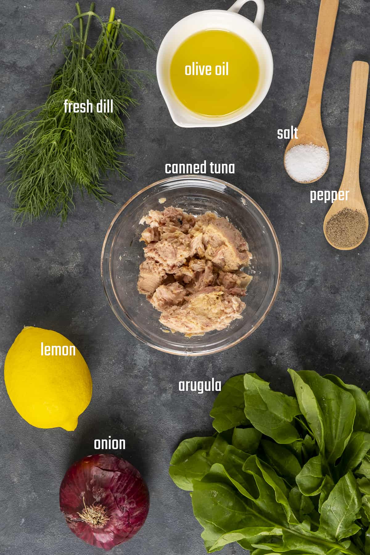 Tuna meat, lemon, onion, fresh dill, arugula, olive oil, salt and pepper on a dark background.