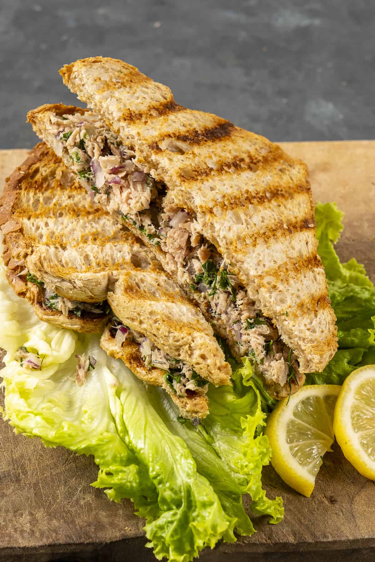 Tuna salad sandwiches accompanied by lettuce leaves and lemon wedges.