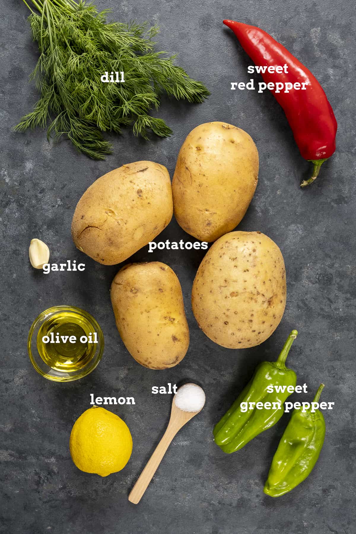 Potatoes, fresh dill, garlic, red pepper, green peppers, lemon and salt on a dark background.