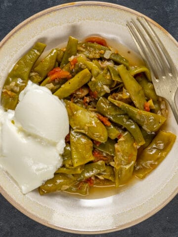 Green beans with tomatoes served in a bowl with some yogurt on the side.