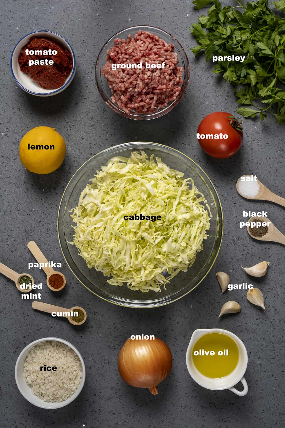 Shredded cabbage, ground beef, tomato paste, garlic, spices, lemon and rice on a dark background.