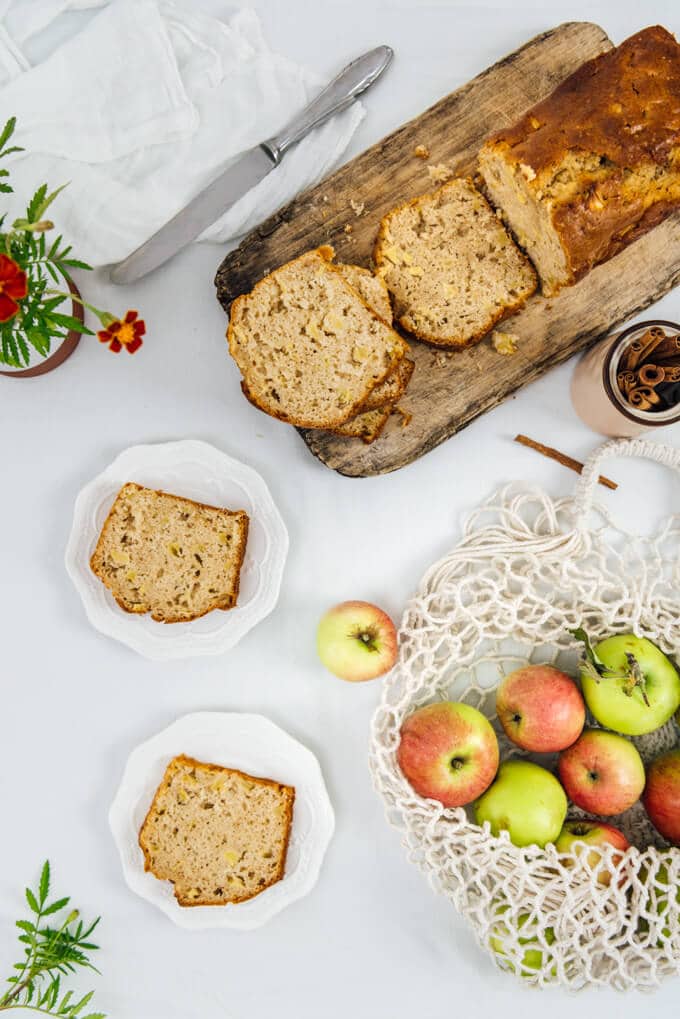 Chunky Apple Cinnamon Bread sliced on a wooden board and served on two white plates, apples in a string bag.