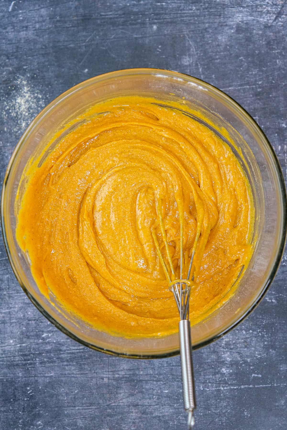 Pumpkind cornmeal muffin batter in a glass mixing bowl and a hand whisk inside it.