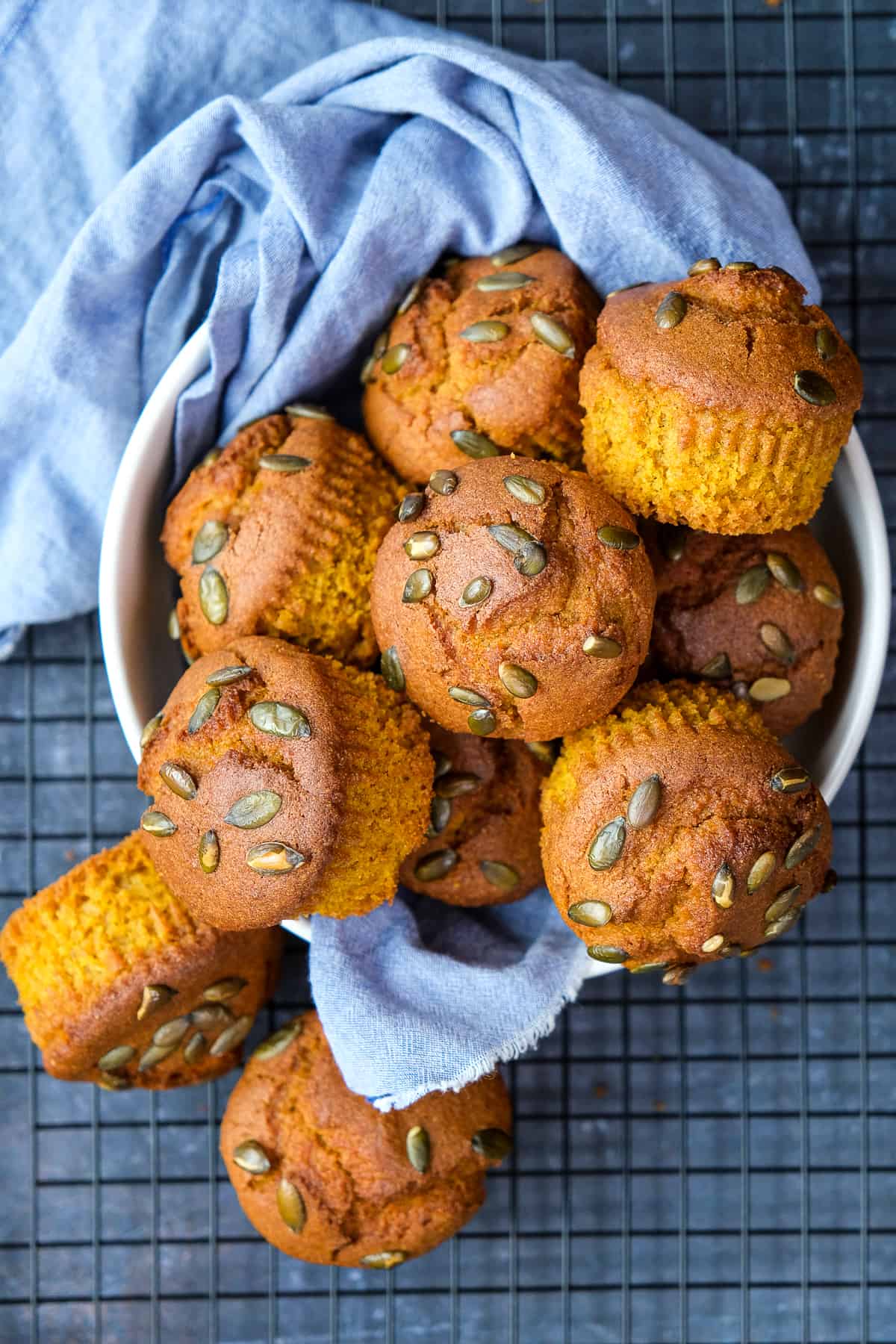 Pumpkin cornbread muffins topped with pumpkin seeds in a white bowl lined with a light blue napkin.
