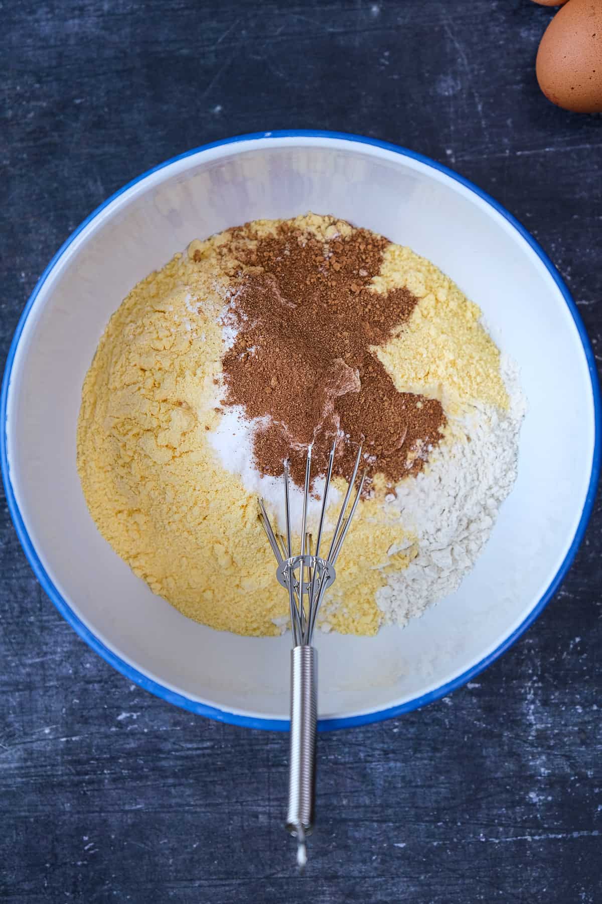 Cornmeal, all purpose flour and pumpkin spice in a white bowl and a hand whisk inside it.