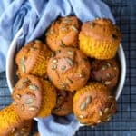 Pumpkin muffins topped with pepitas in a white bowl lined with blue napkin.